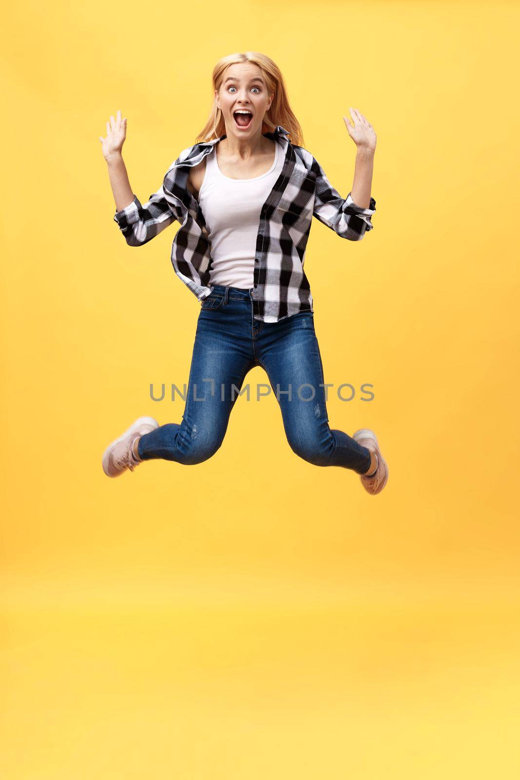 Portrait of surprised young woman in black pants jumping in front of yellow wall. Indoor portrait of young lady in fooling around in studio.