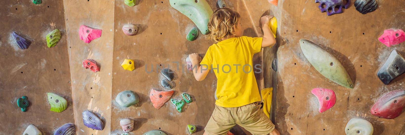 little boy climbing a rock wall in special boots. indoor BANNER, LONG FORMAT by galitskaya