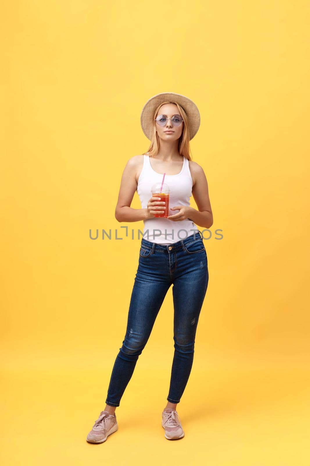 Full length portrait of a cheerful young woman wearing summer clothes while posing and looking at camera isolated over yellow summer background.