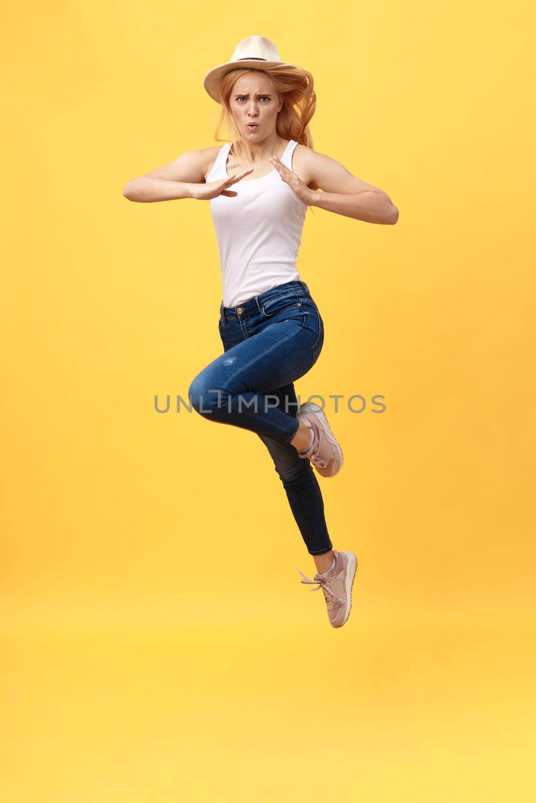 Young woman jump karate kicking in mid air isolated over yellow summer background.