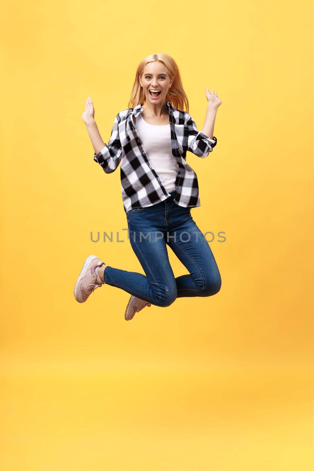 Portrait of surprised young woman in black pants jumping in front of yellow wall. Indoor portrait of young lady in fooling around in studio.