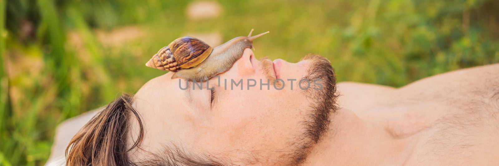 Young man makes a face mask with snail mucus. Snail crawling on a face mask. SPA for man, SPA for all. BANNER, LONG FORMAT