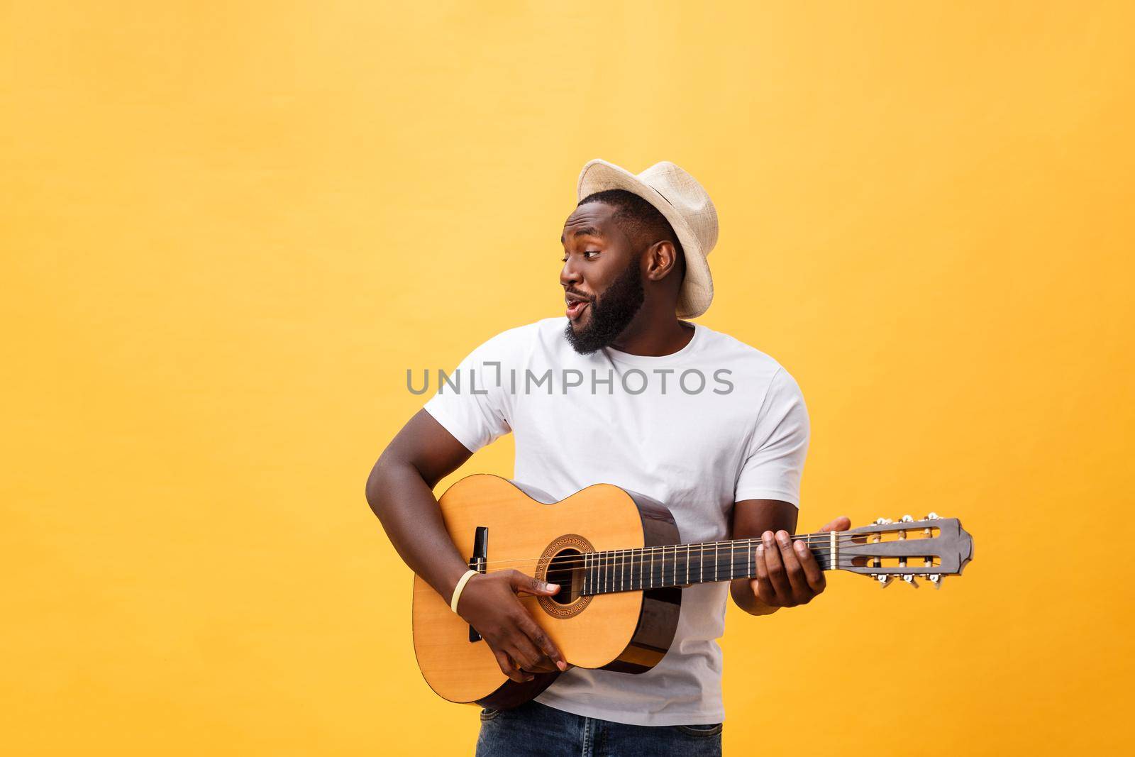 Muscular black man playing guitar, wearing jeans and white tank-top. Isolate over yellow background