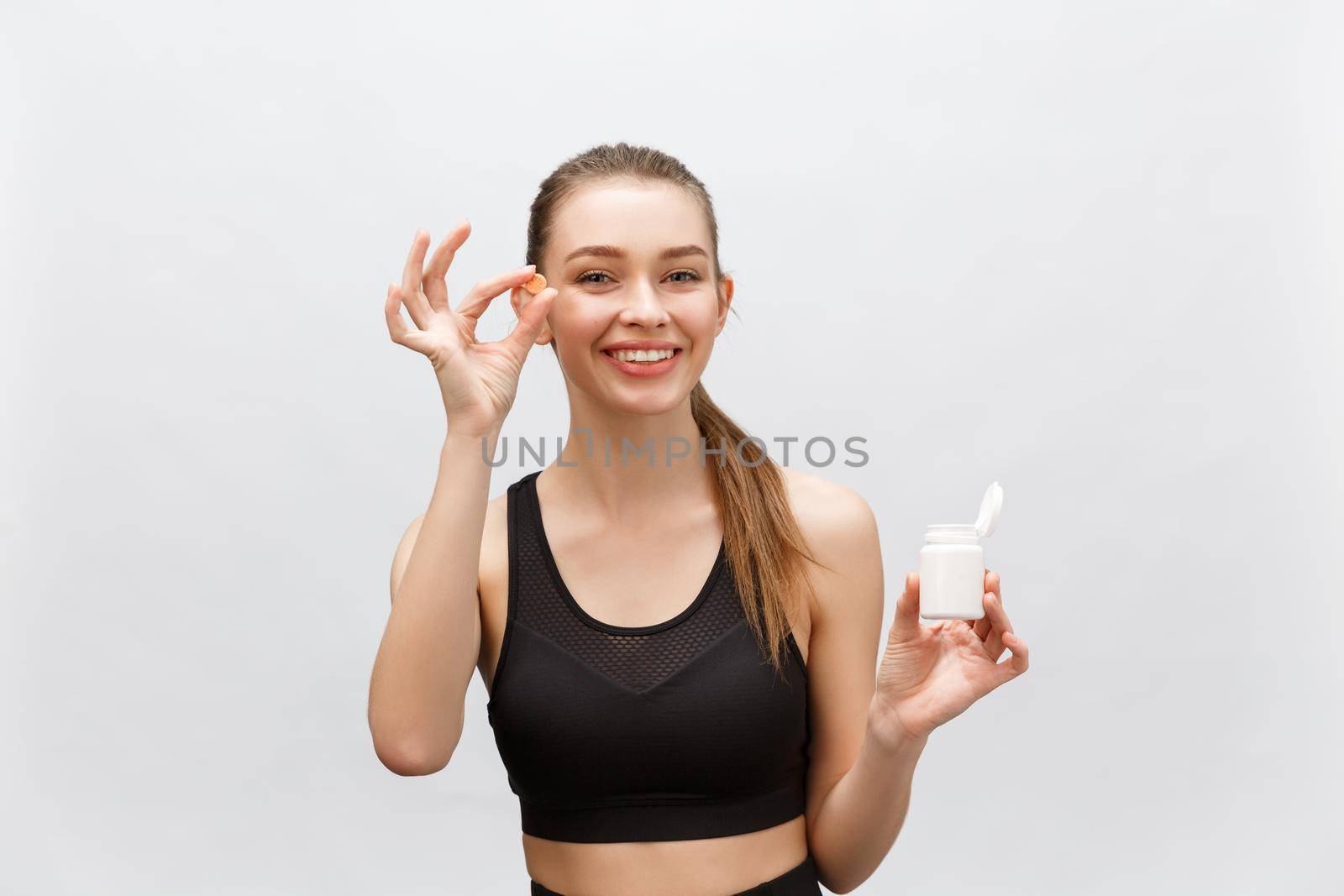 Smiling blonde sport woman holding bottle of medicine on white background.