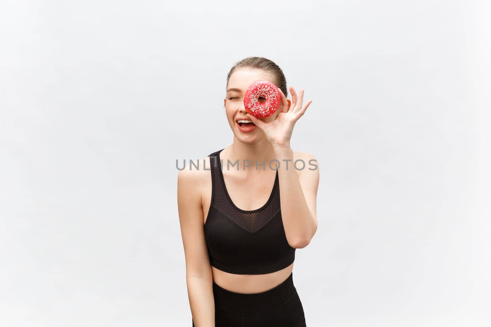 Young beautiful sporty woman in a black undershirt poses and smiles isolated on white background. Girl poses with donut in hands. I have applied donut to the eye.