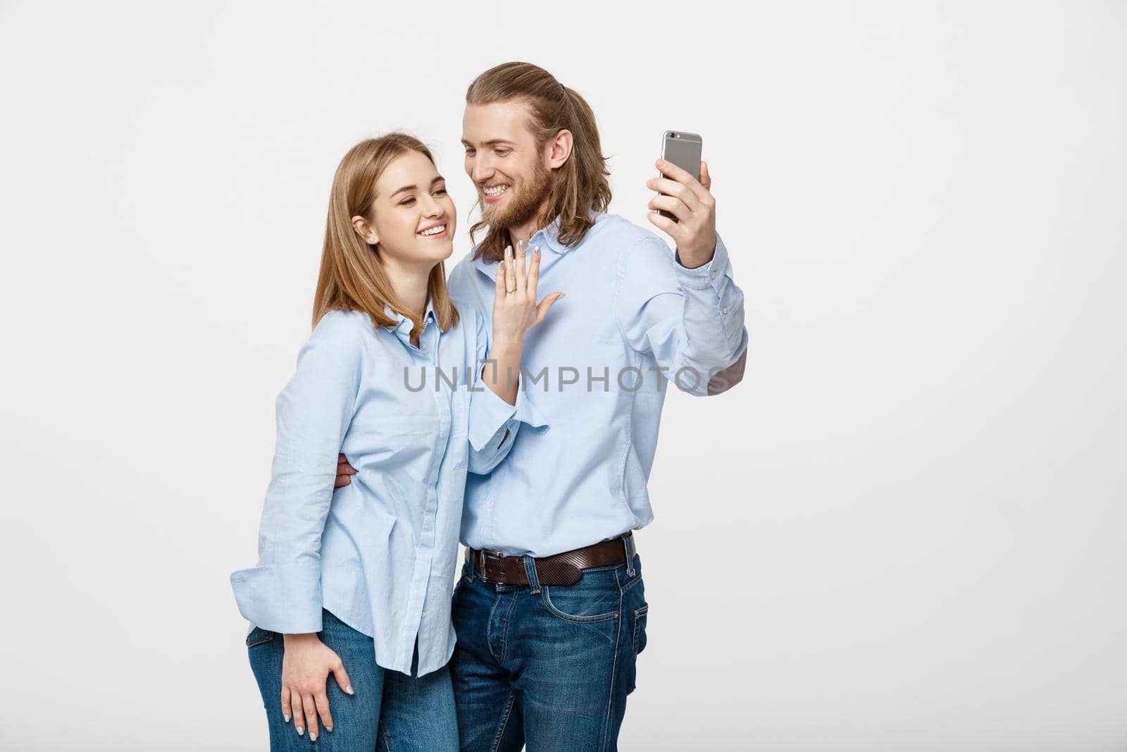 Joyful young loving couple making selfie on camera while standing in white studio background. by Benzoix