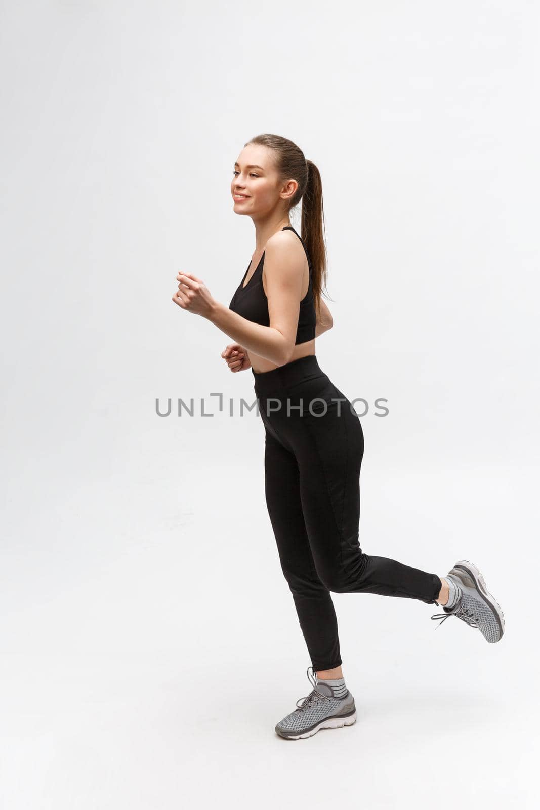 Full length picture of a sports woman running in studio over gray background