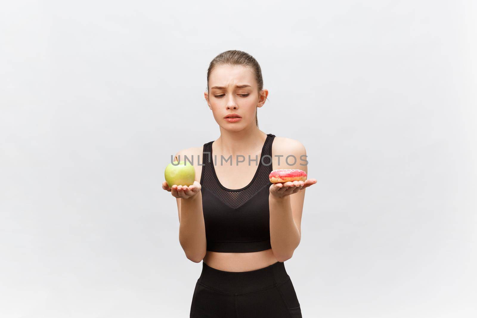 Young woman choosing between donut and apple on white background. Diet food concept by Benzoix