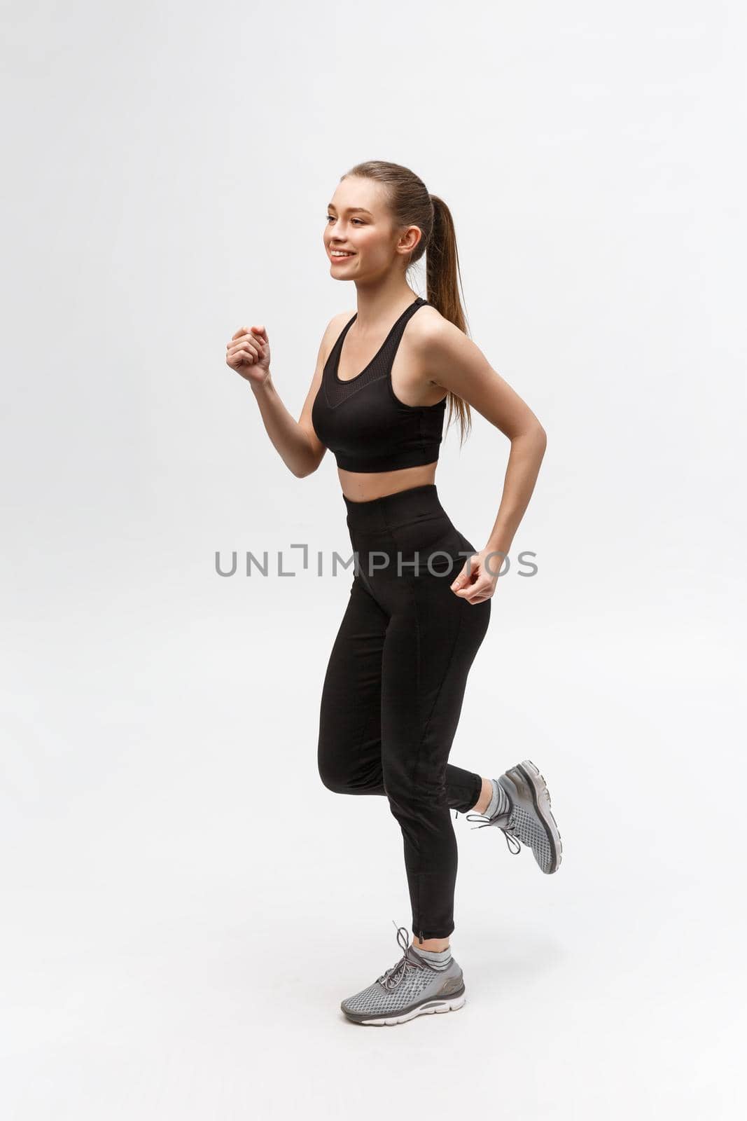 Full length picture of a sports woman running in studio over gray background. by Benzoix