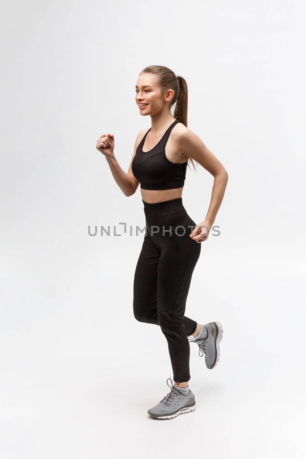Full length picture of a sports woman running in studio over gray background. by Benzoix