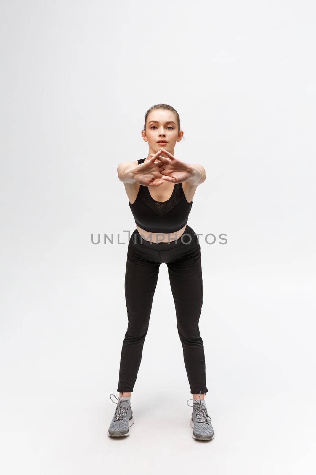 Cheerful healthy girl is stretching herself. She is raising her hands in front with enjoyment. Isolated on white background by Benzoix