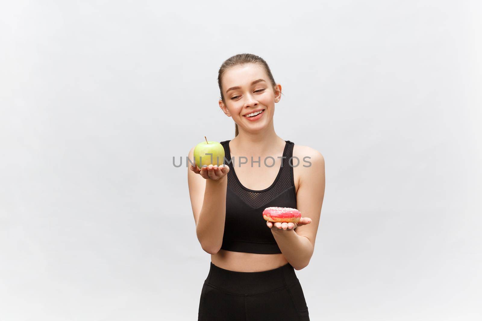 Young woman choosing between donut and apple on white background. Diet food concept.