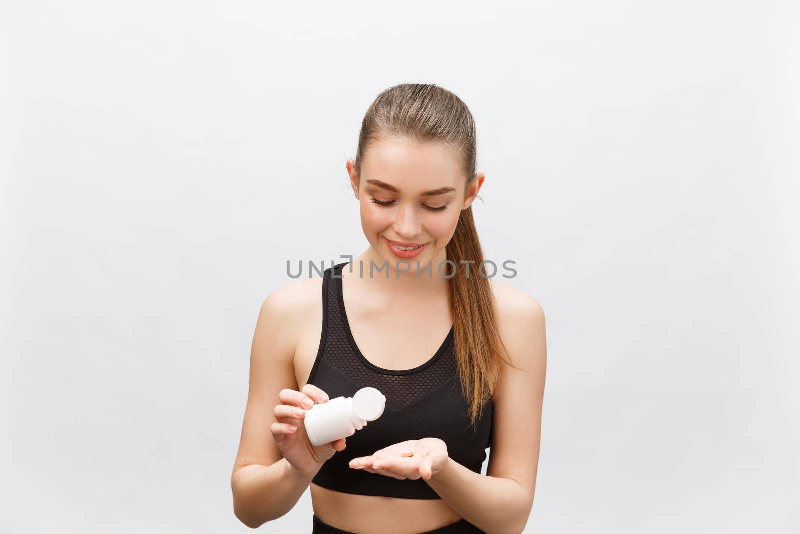 Smiling blonde sport woman holding bottle of medicine on white background.