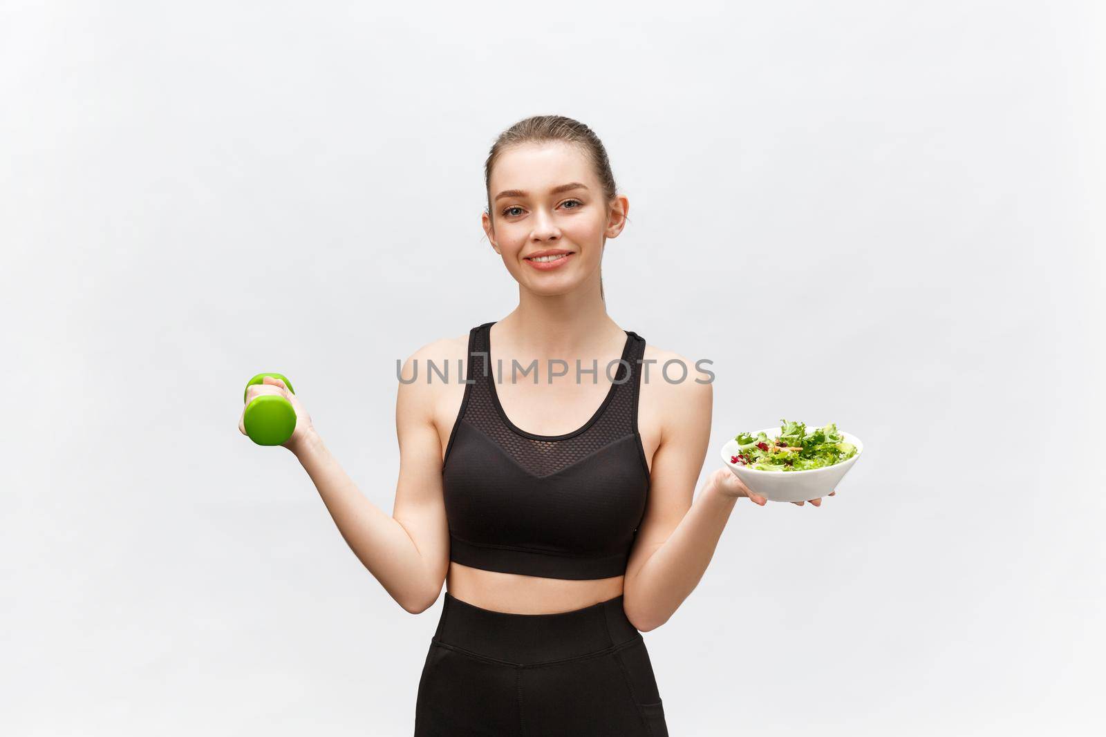 Sport, healthy lifestyle, people concept - young brunette woman with salad and a dumbbell. She is smiling and enjoying the healthy lifestyle. by Benzoix