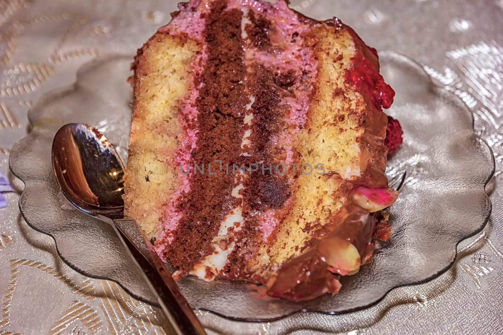 Close view of a delicate piece of chocolate cake, torte with nuts and fruits on a plate with a spoon. 