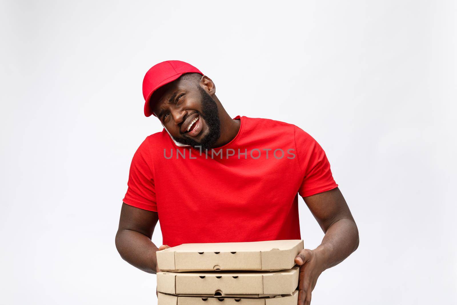 Delivery Concept: Handsome african pizza delivery man talking to mobile with shocking facial expression. Isolated over grey background. by Benzoix