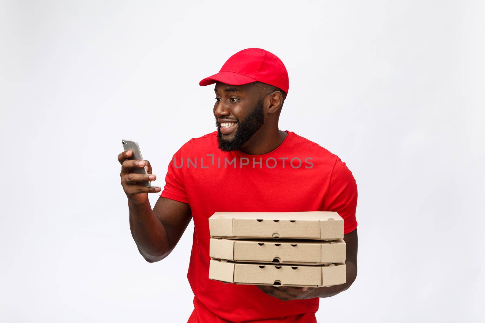 Delivery Concept: Handsome african pizza delivery man talking to mobile with happy facial expression. Isolated over grey background. by Benzoix