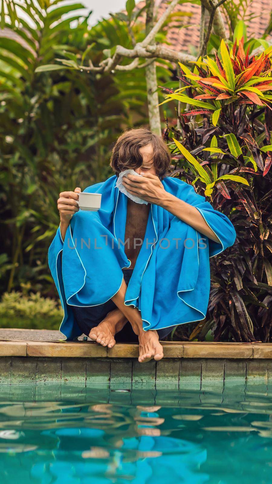 Sick man traveler. The man caught a cold on vacation, sits sad at the pool drinking tea and blows his nose into a napkin. His son is healthy and swimming in the pool. Travel insurance concept. VERTICAL FORMAT for Instagram mobile story or stories size. Mobile wallpaper