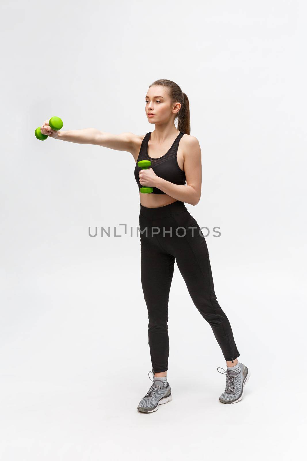 Portrait of Caucasian woman on white background wearing black fitness separate and excercising with dumbells