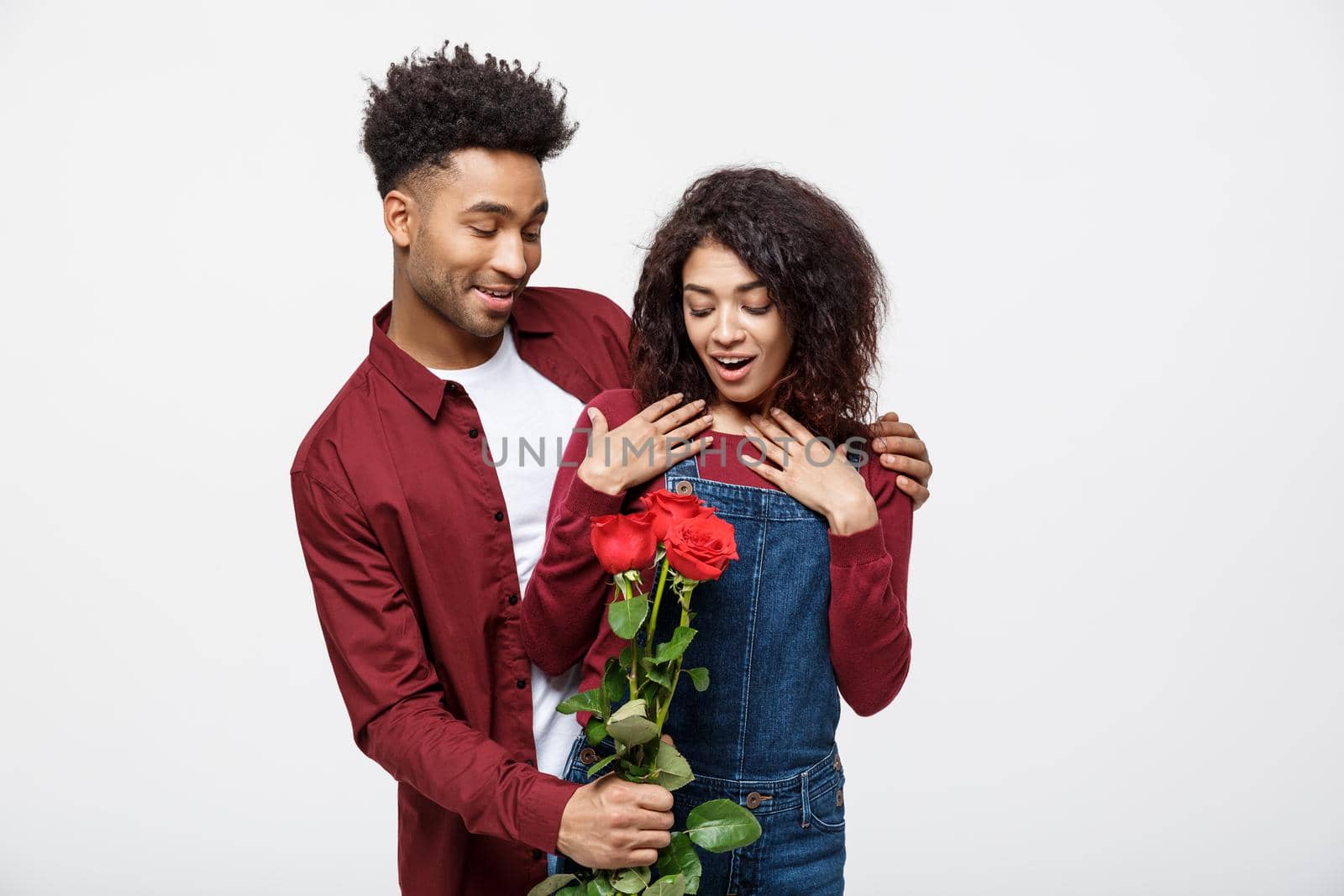 Beautiful elegant couple is hugging and smiling, on gray background. Girl is holding roses by Benzoix