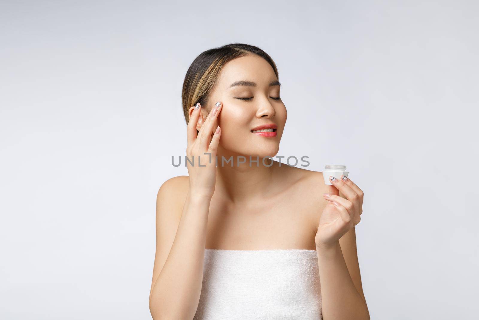 Asian woman applying cosmetic cream on skin on isolated white background.