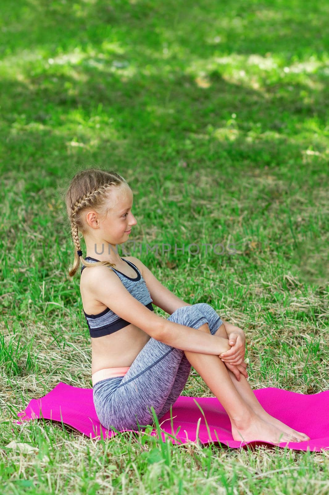 Little girl is sitting on a roll mat wearing sportswear in the public park.