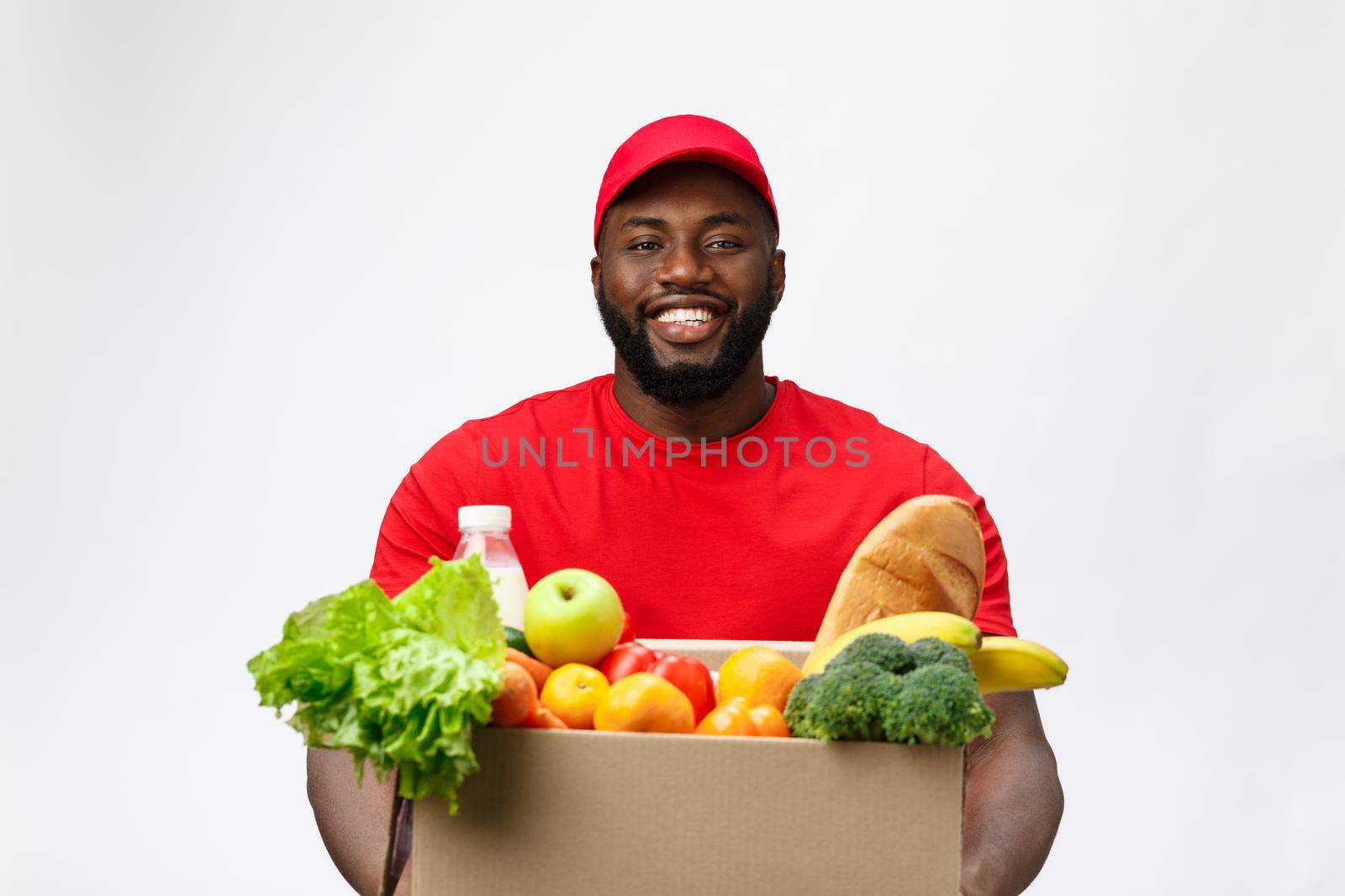Delivery Concept - Handsome African American delivery man carrying package box of grocery food and drink from store. Isolated on Grey studio Background. Copy Space.