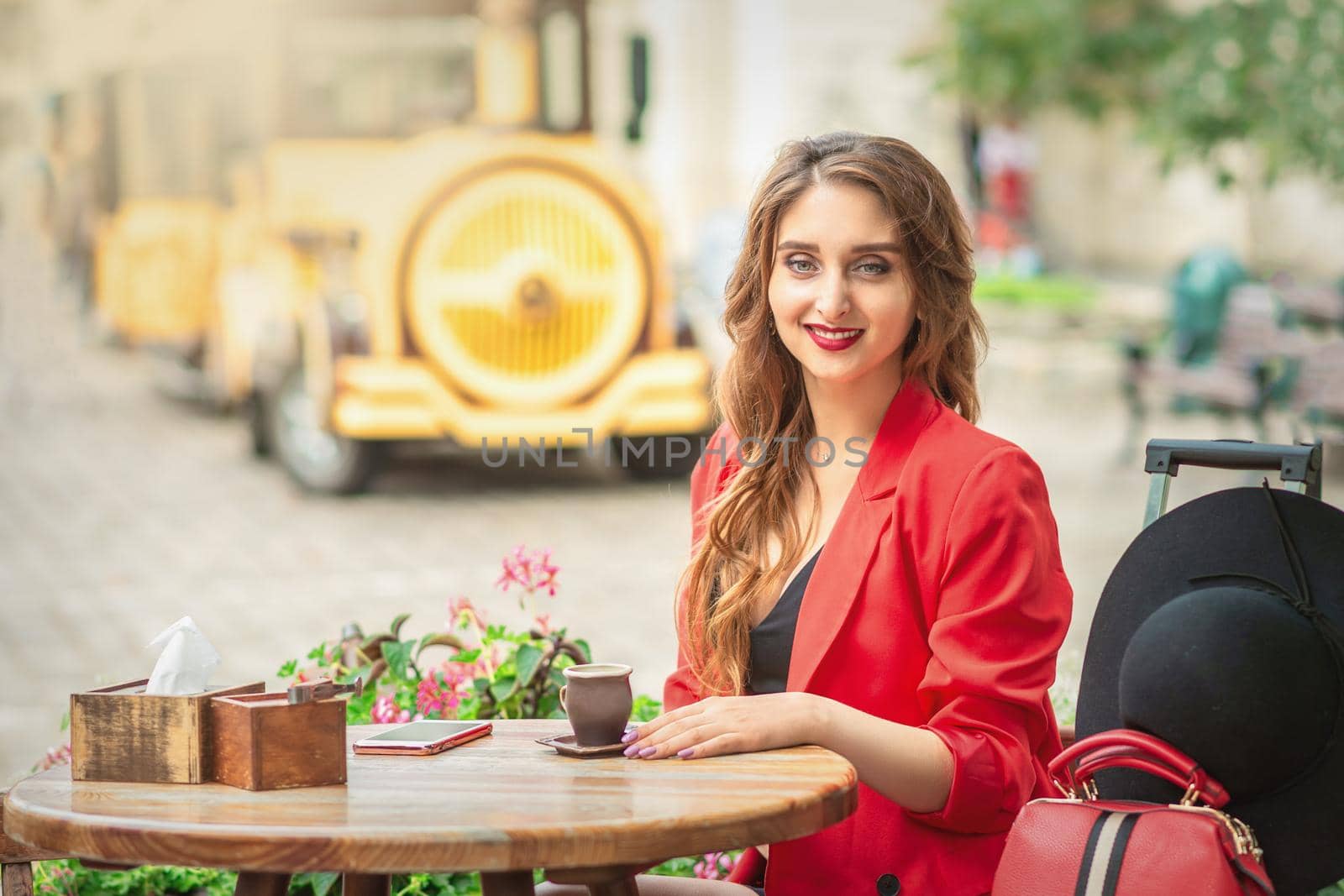 Outdoor portrait of young beautiful woman sitting at the table with cup of coffee and smartphone in the street.