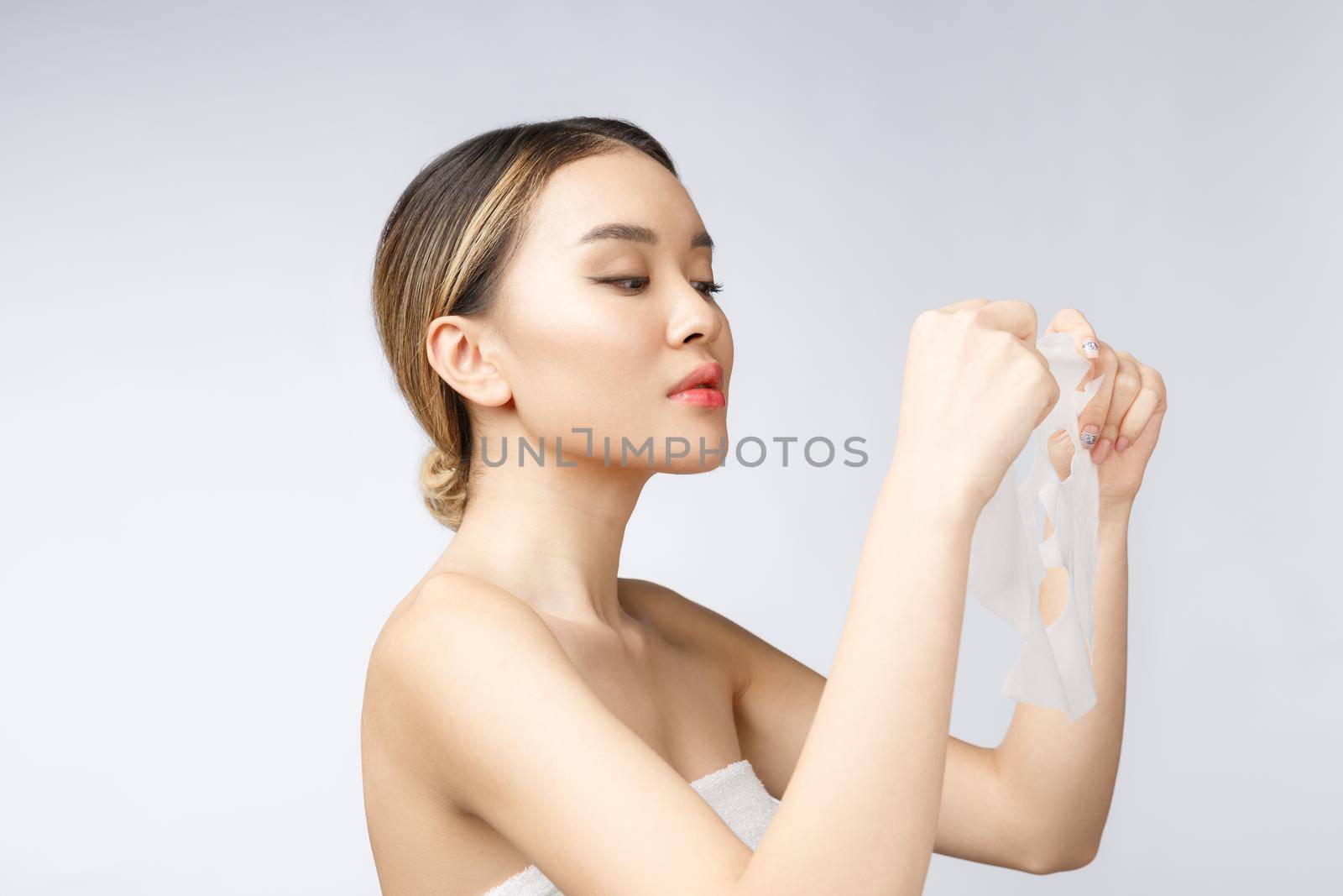 Beautiful asian woman applying paper sheet mask on her face white background.