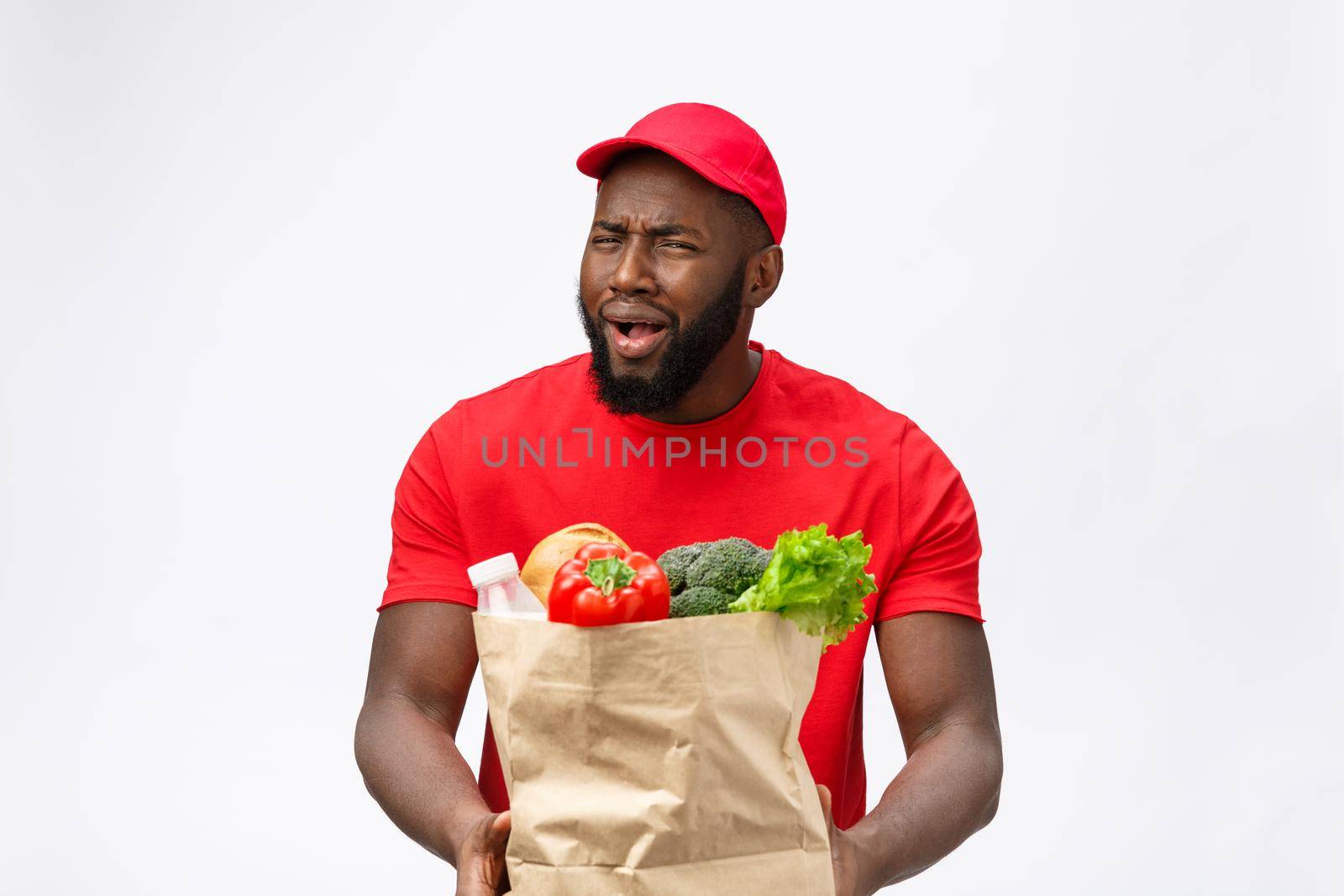 Delivery Concept - Portrait of Serious African American delivery man showing silly aggressive expression and unhappy. Isolated on Grey studio Background. Copy Space