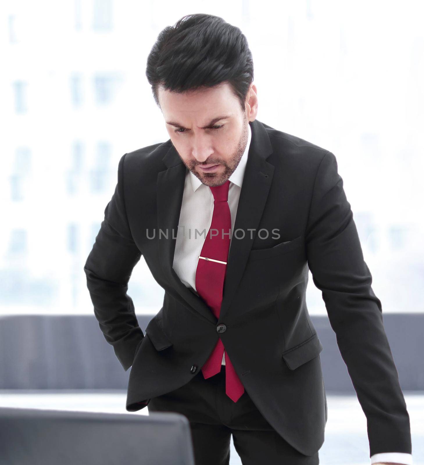 Businessman standing at his Desk and looking at the laptop screen by asdf