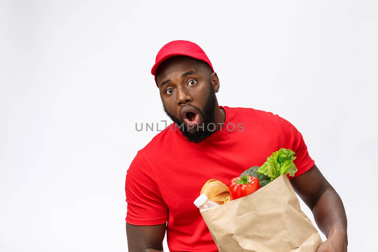 Young african american man holding grocery package in hands with shocking face. Isolated over Grey background