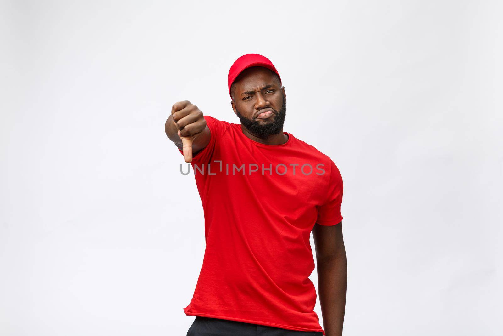 Delivery Concept - Portrait of Serious African American delivery man showing silly aggressive expression and unhappy. Isolated on Grey studio Background. Copy Space. by Benzoix