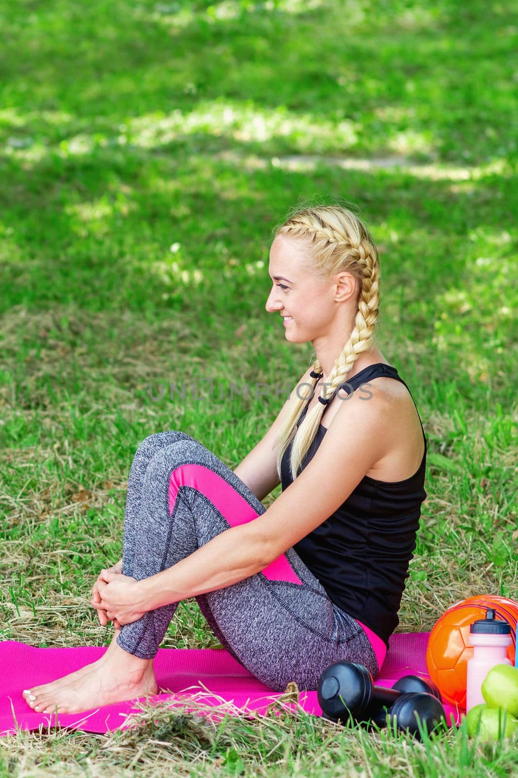 Young woman is sitting on a roll mat wearing sportswear in the public park.