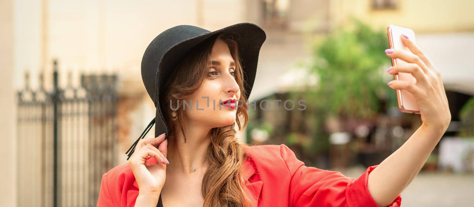 Stylish young woman is taking selfie walking on the street of old European city.