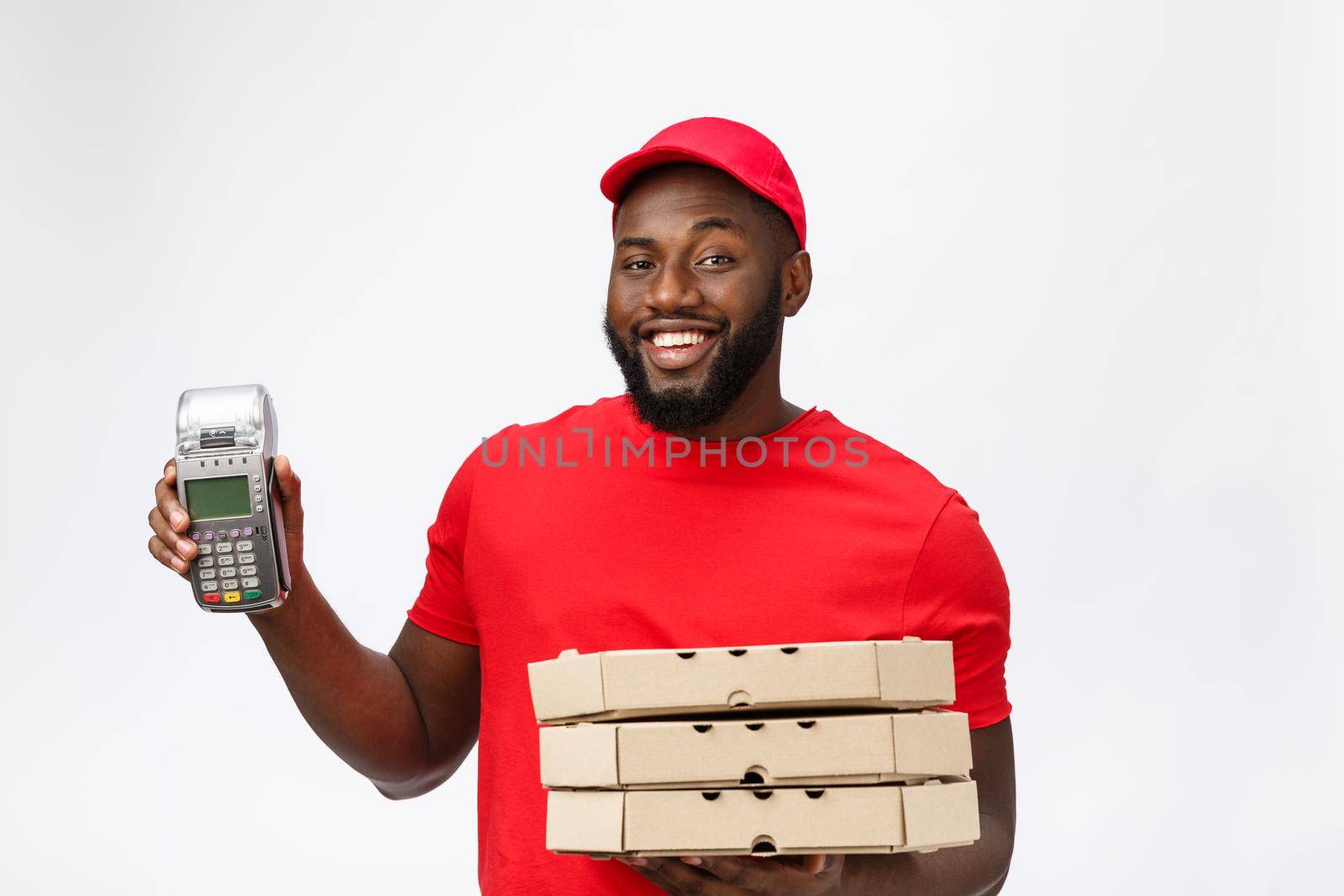 Happy young African American delivery man holding up an electronic card payment machine and delivery product. Isolated over grey background by Benzoix