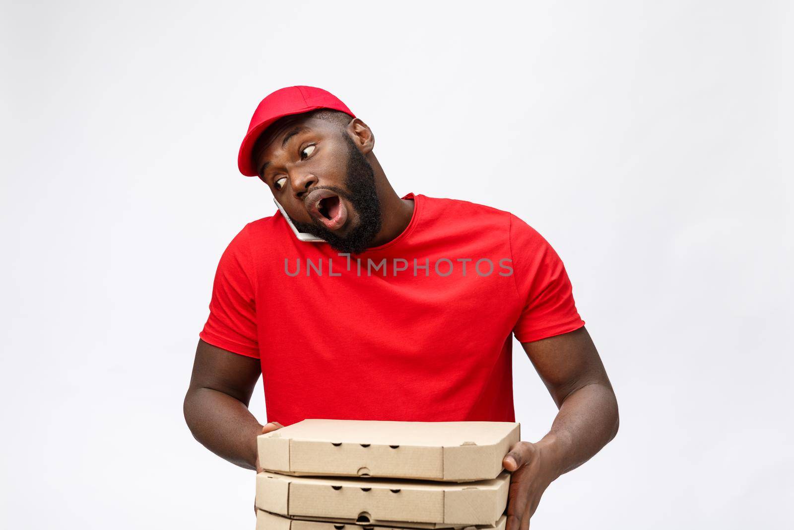 Delivery Concept: Handsome african pizza delivery man talking to mobile with shocking facial expression. Isolated over grey background