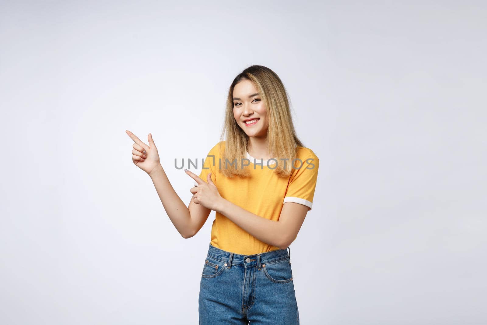 Beautiful young Asian woman pointing her finger up with cheerful expression, on white background
