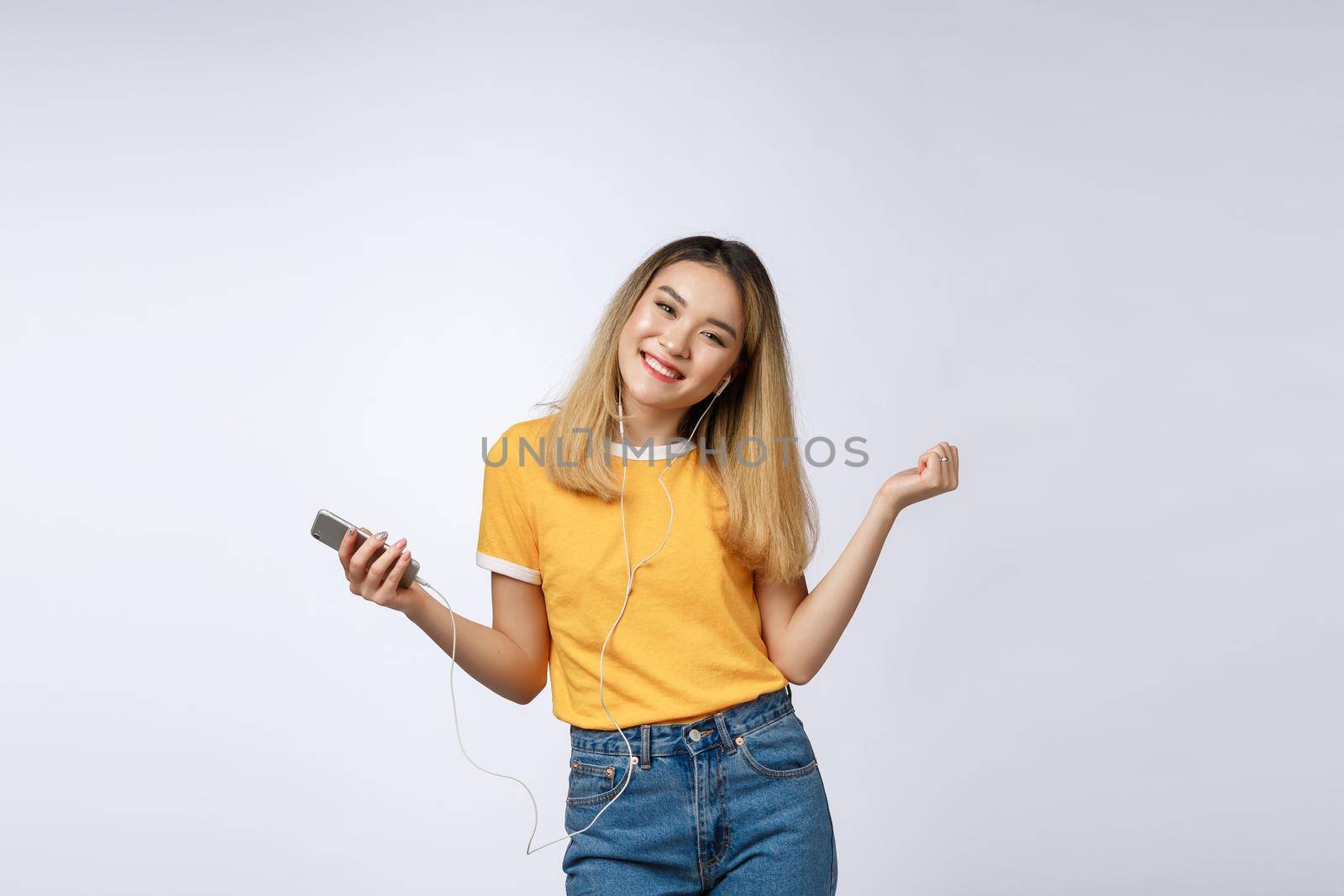 Portrait of a joyful satisfied asian woman in headphones listening to music and jumping isolated over white background by Benzoix