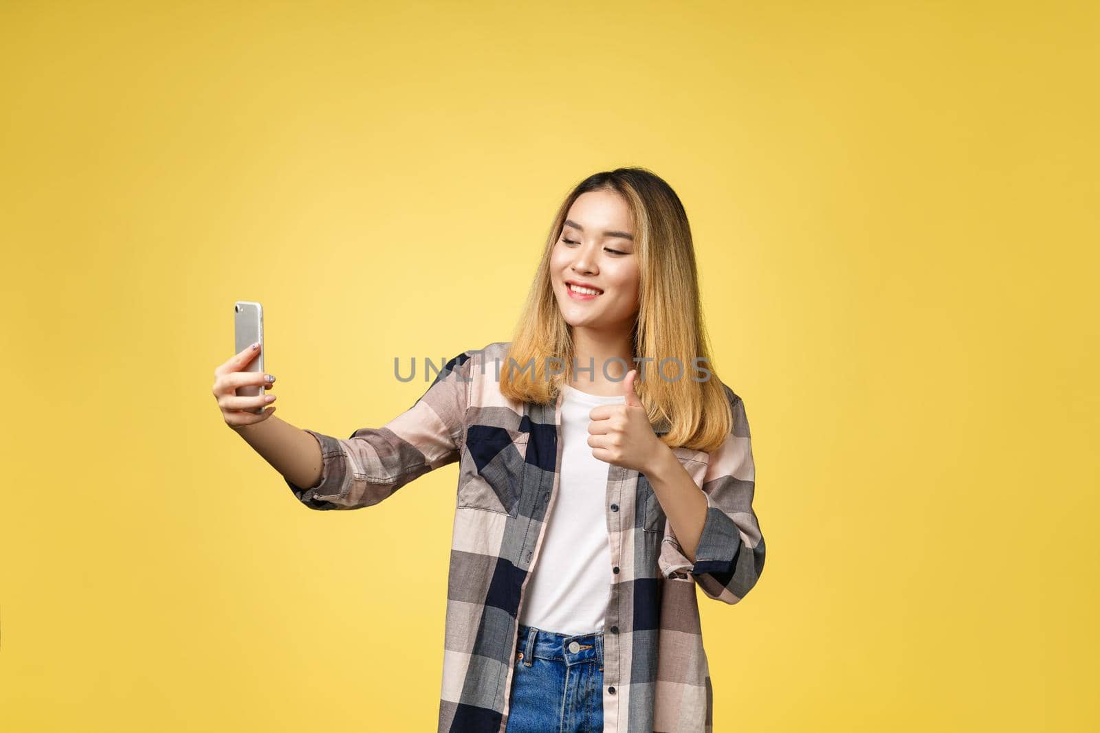 Pretty girl take a self portrait with her smart phone. Asian girl selfie, isolated on yellow background. by Benzoix