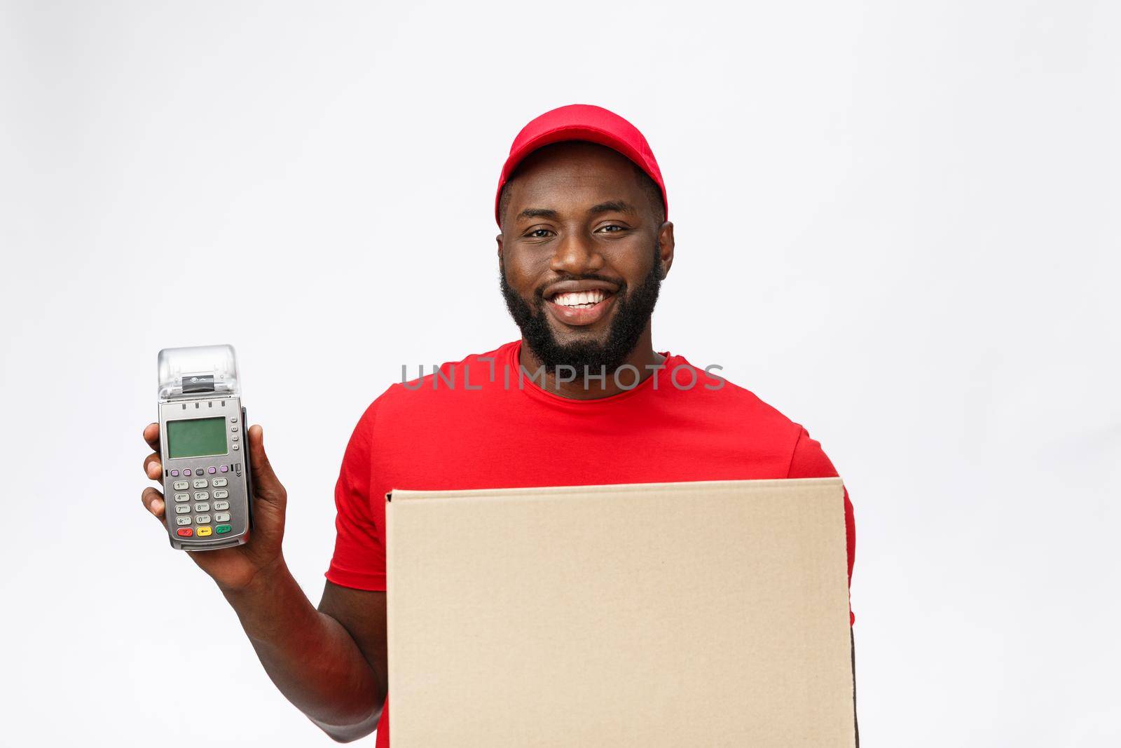 Happy young African American delivery man holding up an electronic card payment machine and delivery product. Isolated over grey background by Benzoix