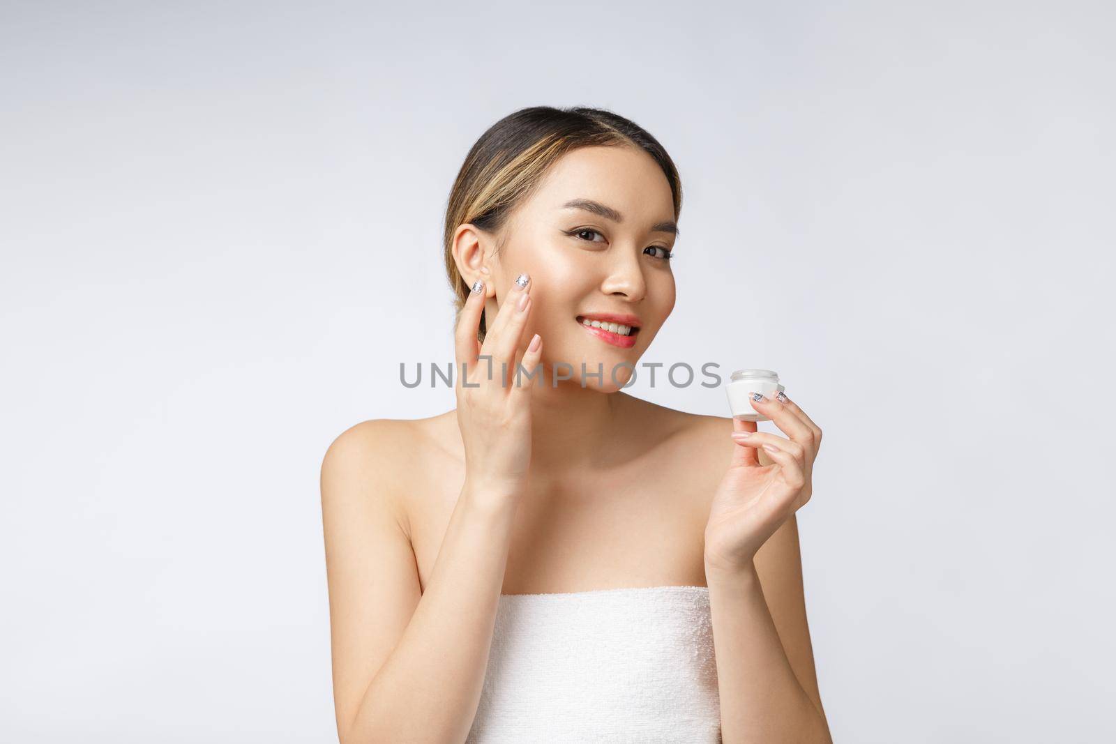 Asian woman applying cosmetic cream on skin on isolated white background.