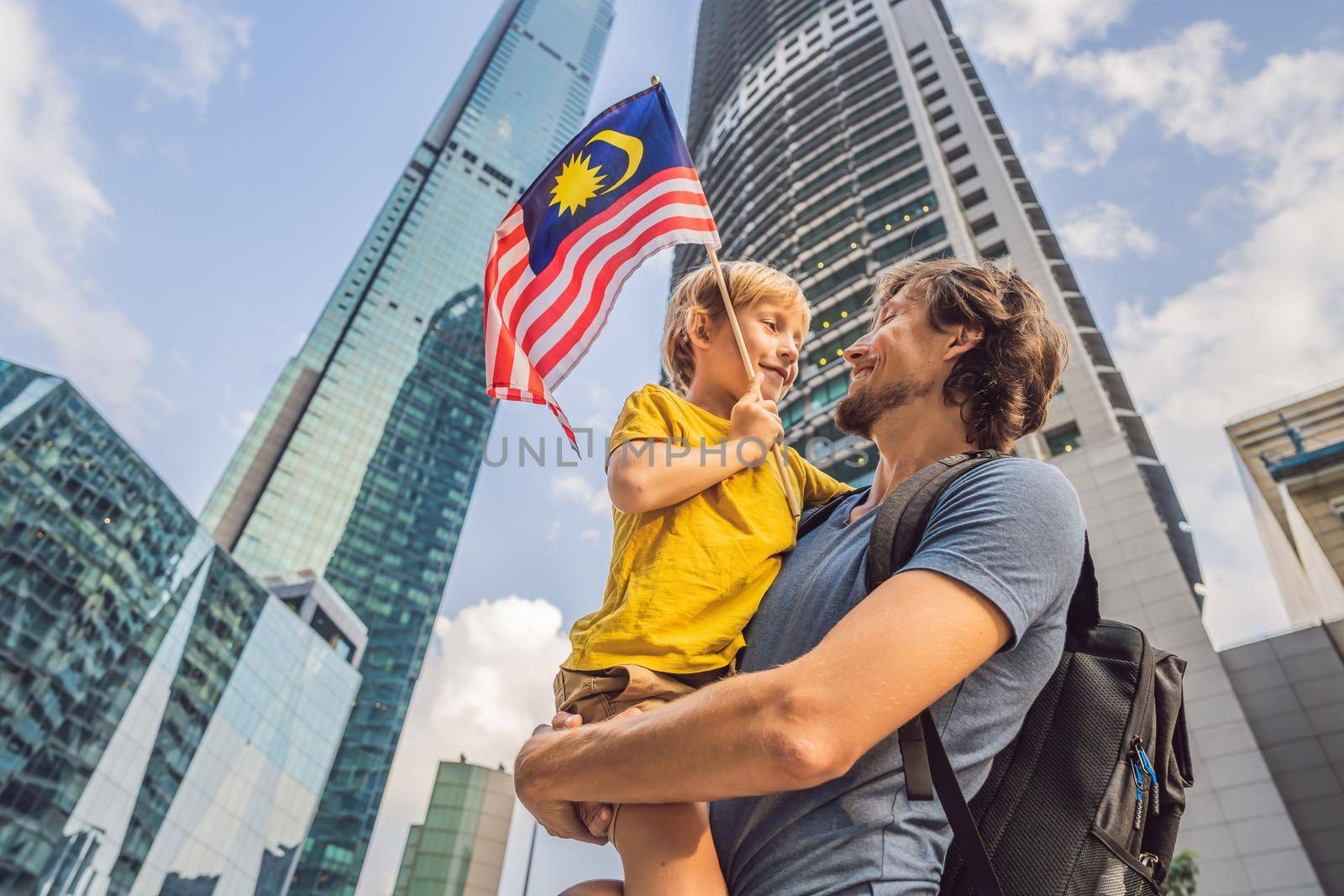 Dad and son tourists in Malaysia with the flag of Malaysia near the skyscrapers. Traveling with kids concept.