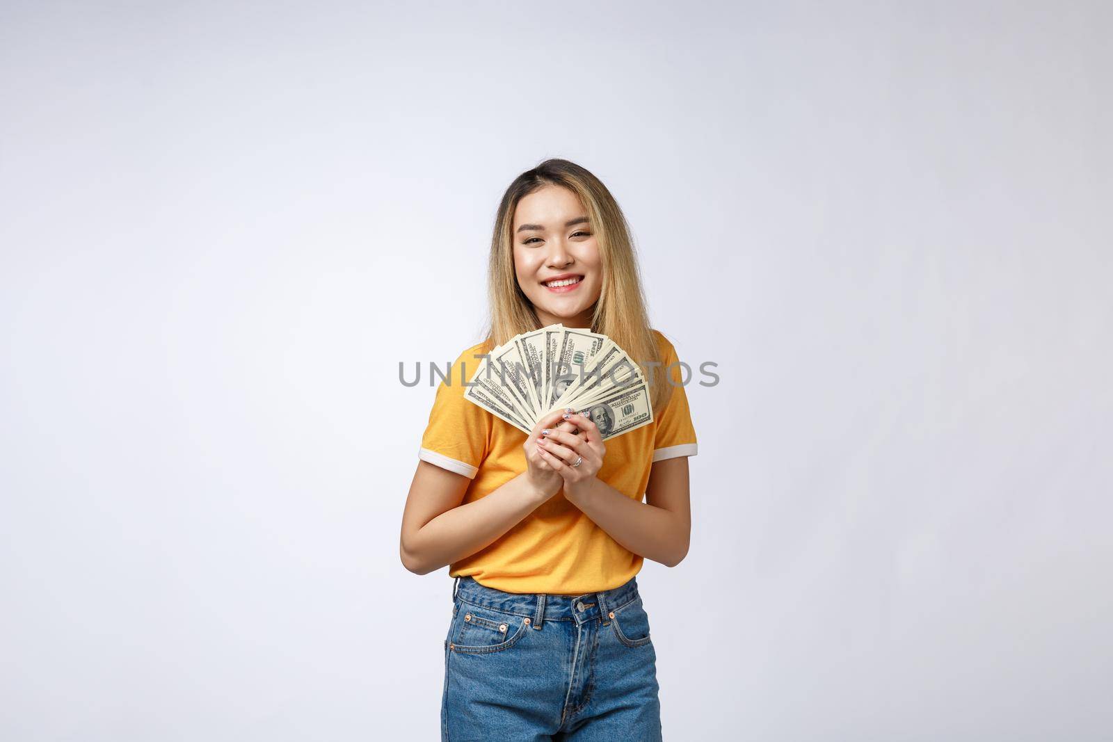 Asian woman holding cash notes isolated in white background. Young asian woman in white t-shirt in winning surprise, holding dollar note. Young rich hipster concept