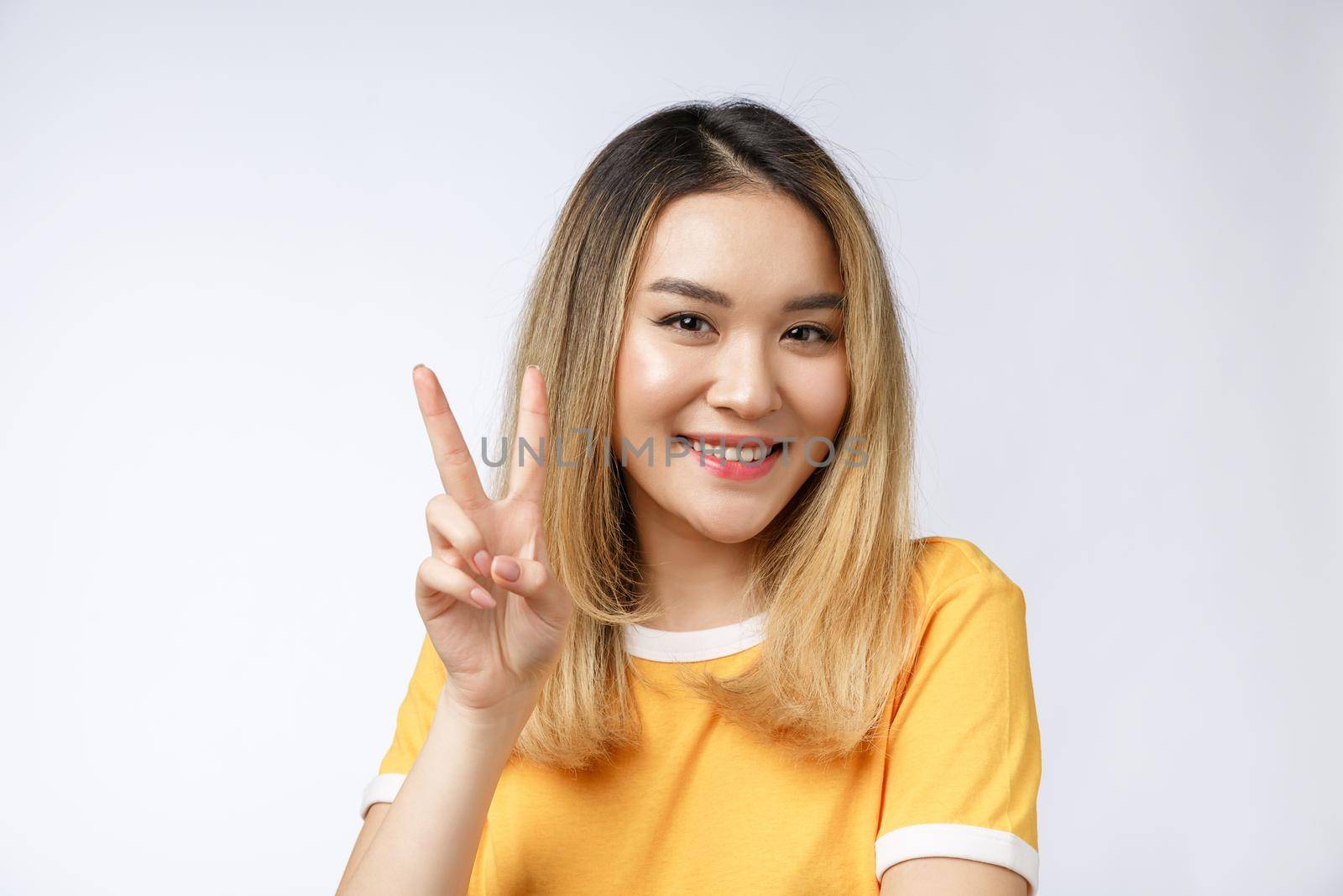 Happy young asian woman showing two fingers or victory gesture with blank copyspace area for text,Portrait of beautiful Asian woman. by Benzoix
