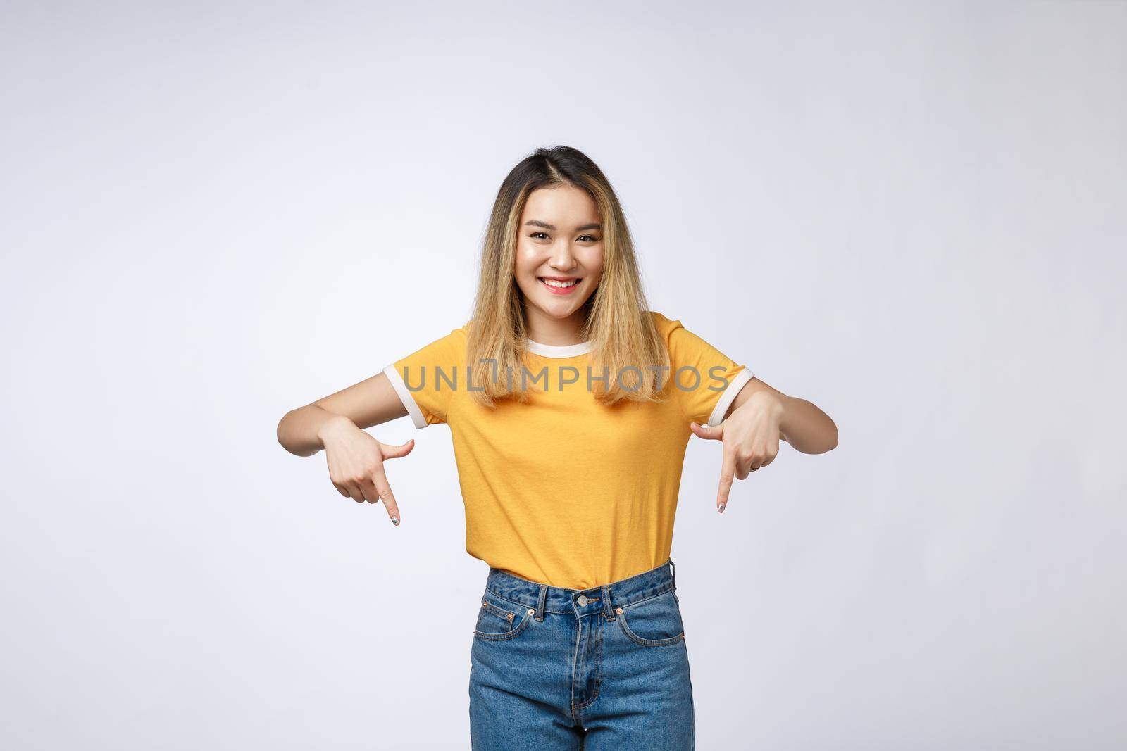 Beautiful young Asian woman point down to blank space on grey background