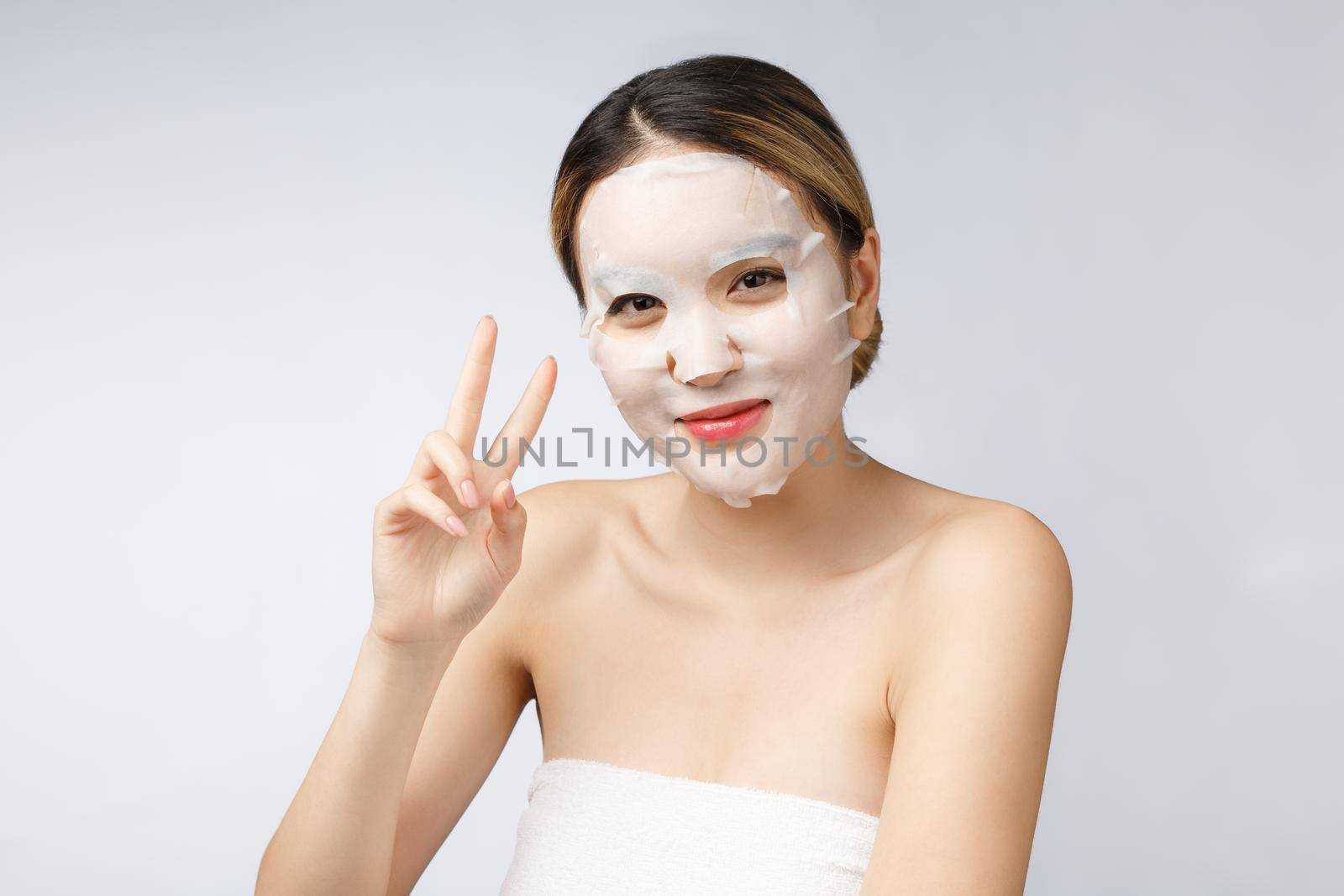 Beautiful asian woman applying paper sheet mask on her face white background
