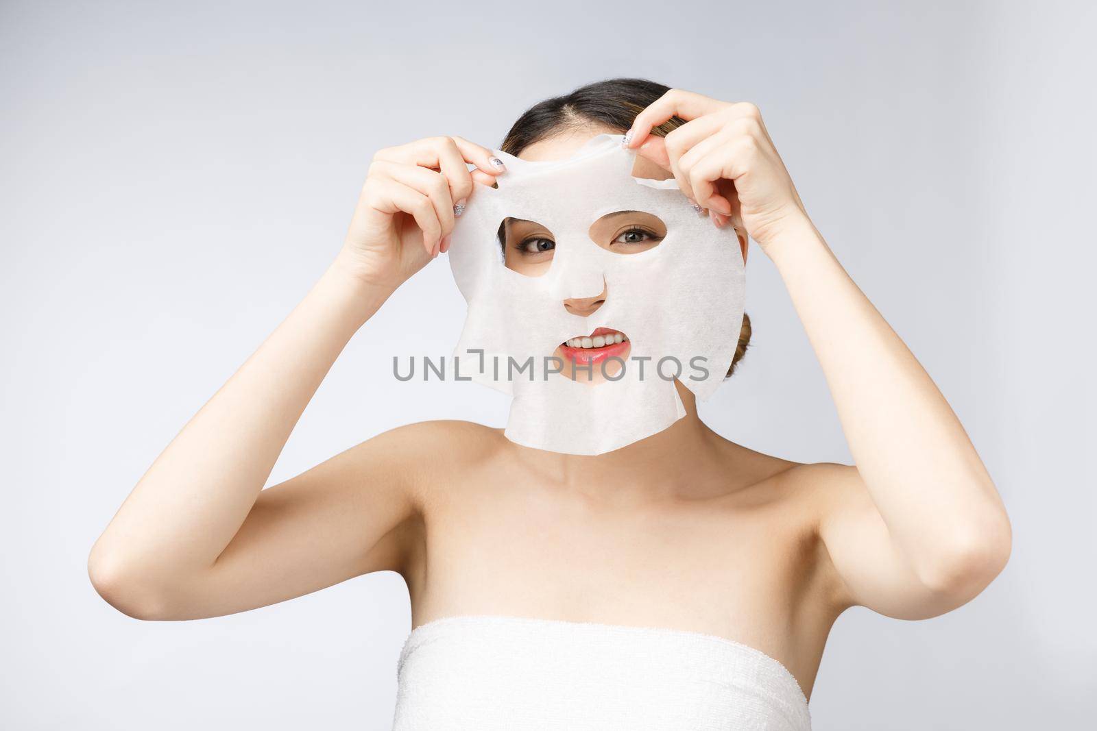 Beautiful asian woman applying paper sheet mask on her face white background by Benzoix