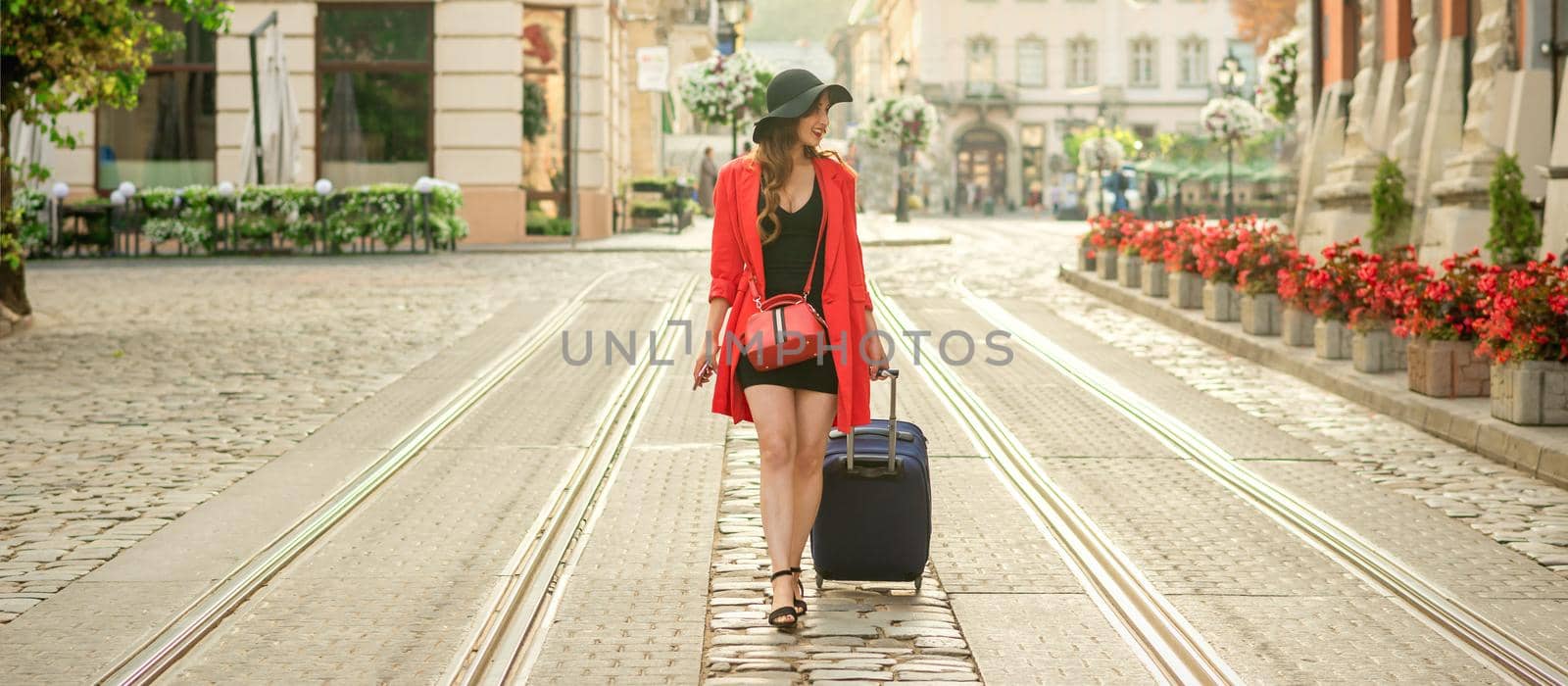 Beautiful young business woman walking on the tram track of a city street with blue travel bag.