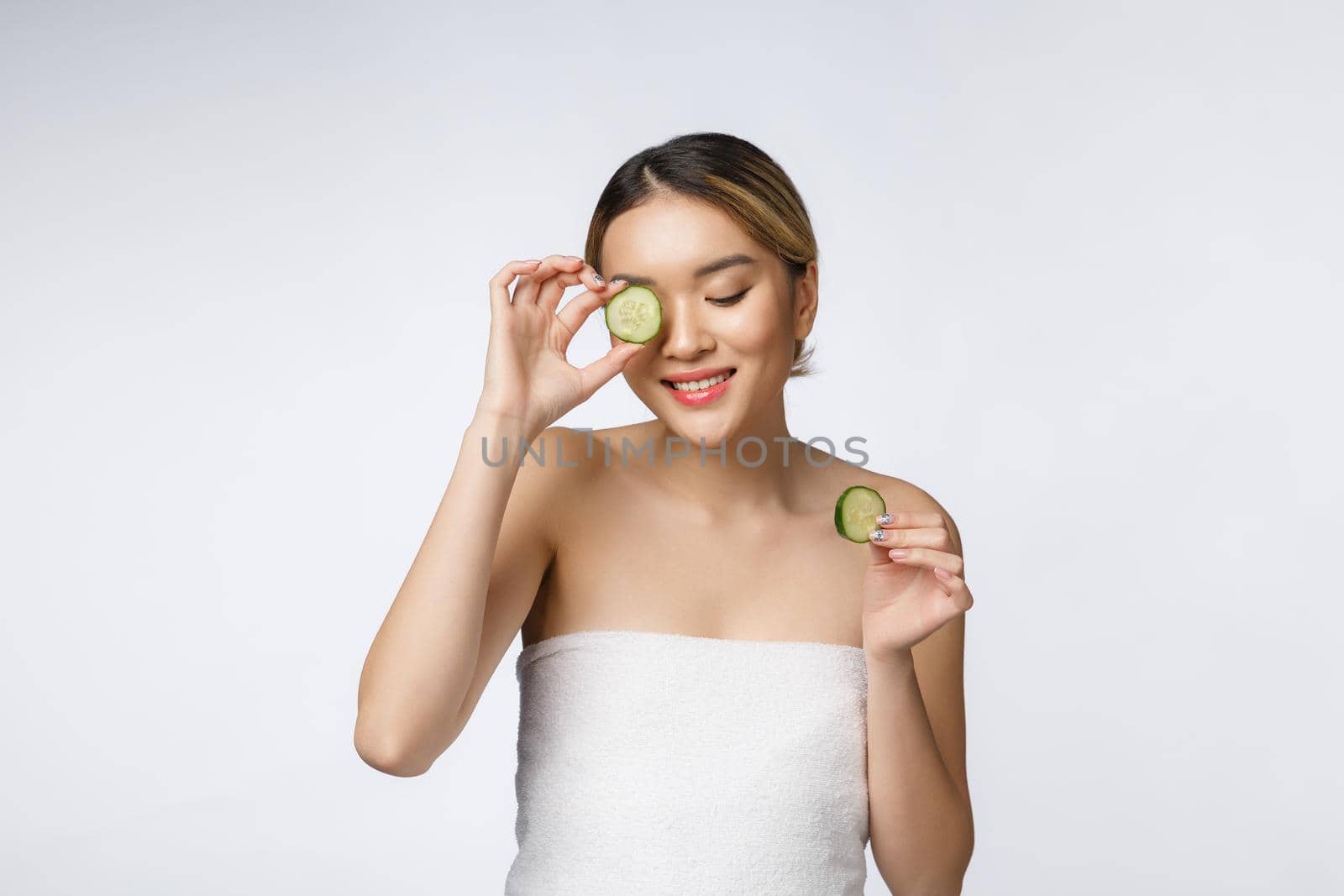 Young asian woman with cucumber slice in her hands isolated on white background